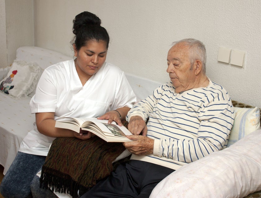 The carer assist an elderly in reading books.