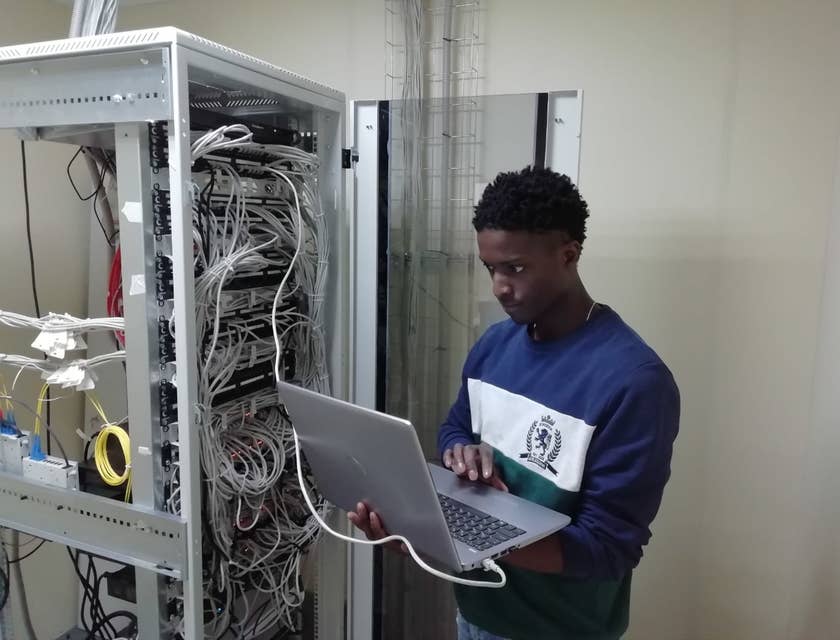 Certified Ethical Hacker holding his laptop while connected to the server and doing penetration tests to the system