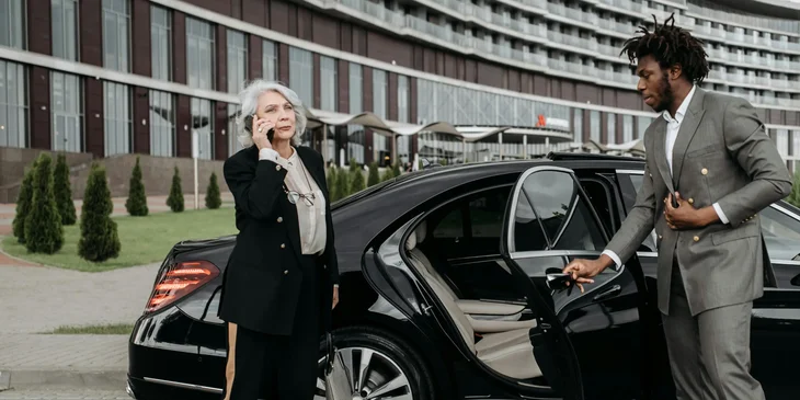 A chauffeur standing outside a vehicle assisting a VIP client.