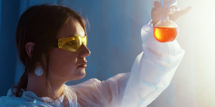 female Chemical Engineer looking at a glass vial containing an orange-colored liquid