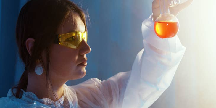 female Chemical Engineer looking at a glass vial containing an orange-colored liquid