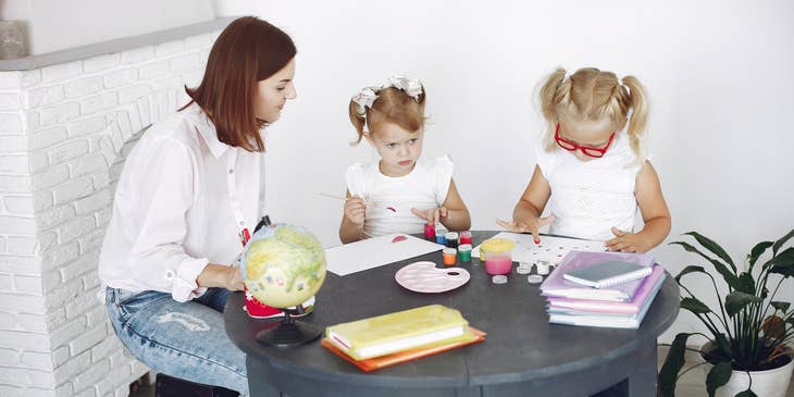 Childcare Worker looking after two girls painting at the table