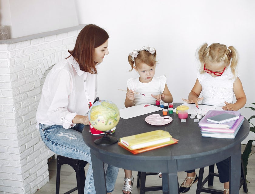 Childcare Worker looking after two girls painting at the table