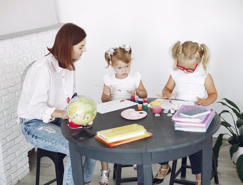 Childcare Worker looking after two girls painting at the table