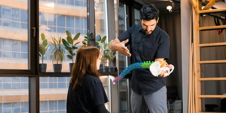 A chiropractor holding a spine model tool and discussing it to a patient.