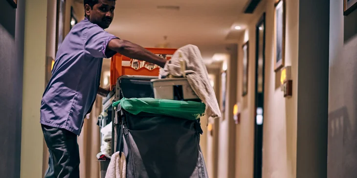 A cleaner with his utility cart in a hallway.