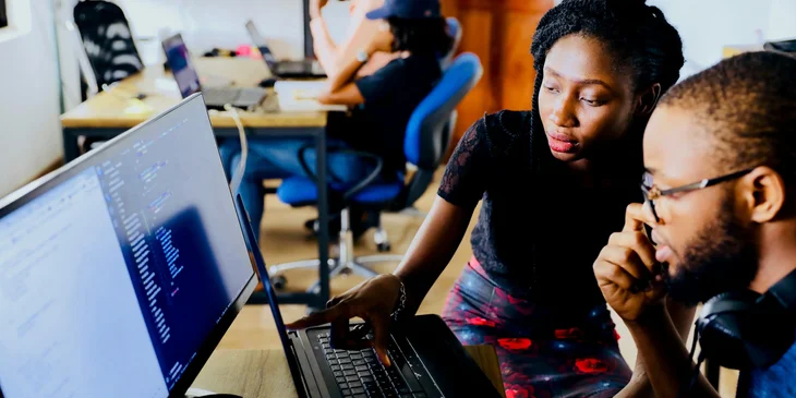 A client services manager sitting and pointing out something on the laptop while her male coworker looks on.