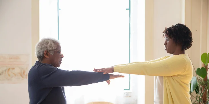 A female CNA helping an elderly with his exercise routine.