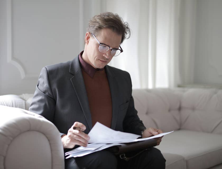 A Compliance Auditor sitting in a white couch reviewing and analyzing some company records.