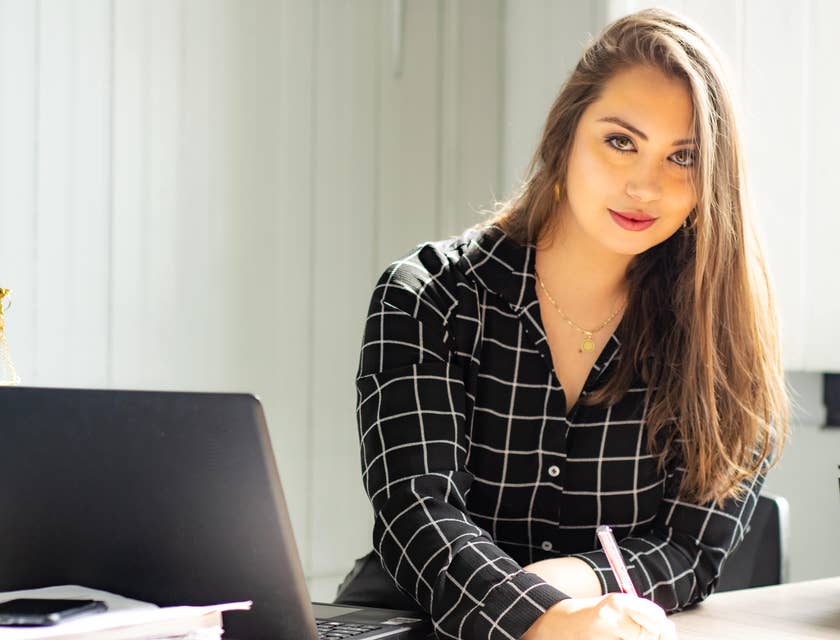 Compliance Engineer sitting on her workstation with an open laptop and signing papers on her desk