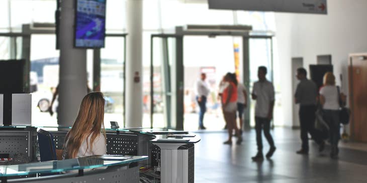 female Concierge sitting at the reception desk and looking over at the building's entrance