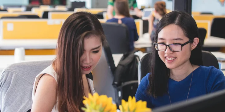 A creative technologists sitting together on a desk and discussing a detail on the project they are both working on.