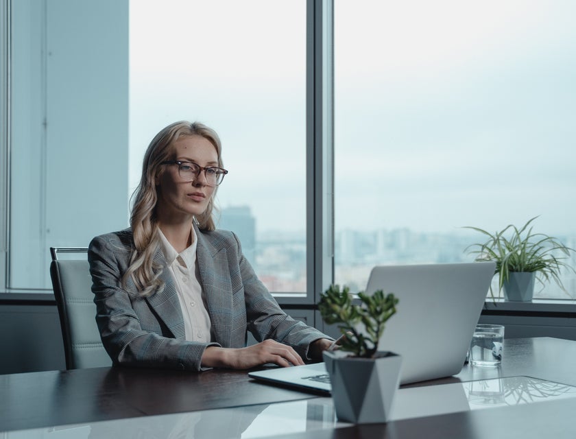 Credit Manager wearing a gray blazer and sitting on an office desk while looking at her laptop
