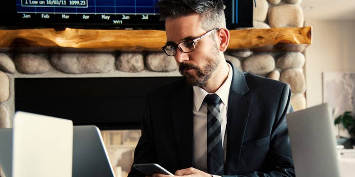 Credit Specialist wearing a business suit and holding his phone while looking at his laptop