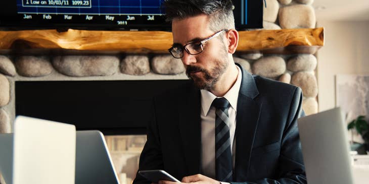Credit Specialist wearing a business suit and holding his phone while looking at his laptop