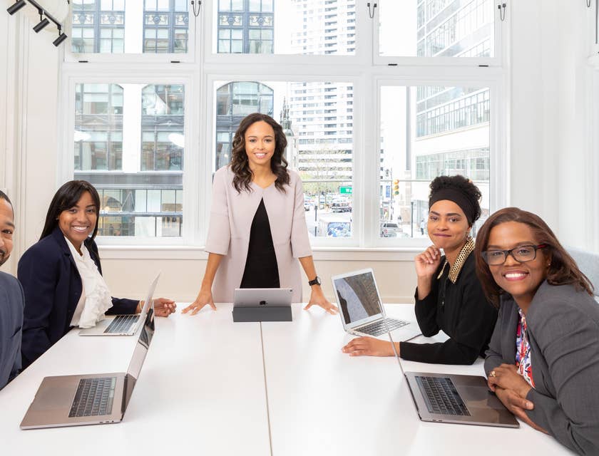 female Customer Service Coordinator smiling and standing while the rest of her team members are sitting inside the meeting room