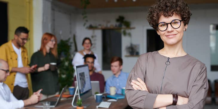 female Customer Service Manager smiling while her team on the background is on break