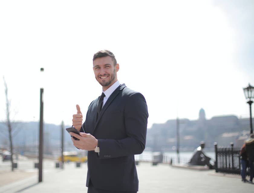 Customer Success Manager smiling and wearing a business suit while giving a thumbs up and holding his mobile phone