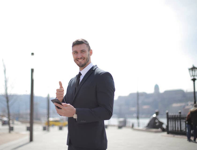 Customer Success Manager smiling and wearing a business suit while giving a thumbs up and holding his mobile phone