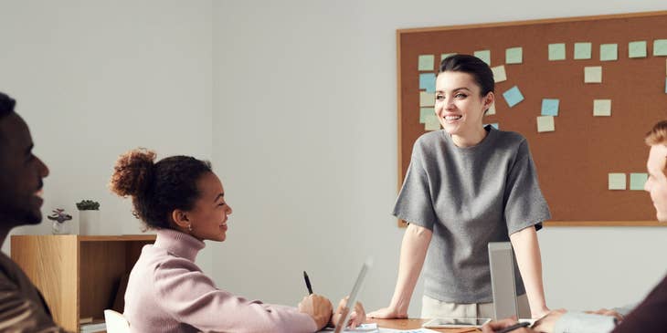 Customer Support Executive standing in the meeting room in front of the team.
