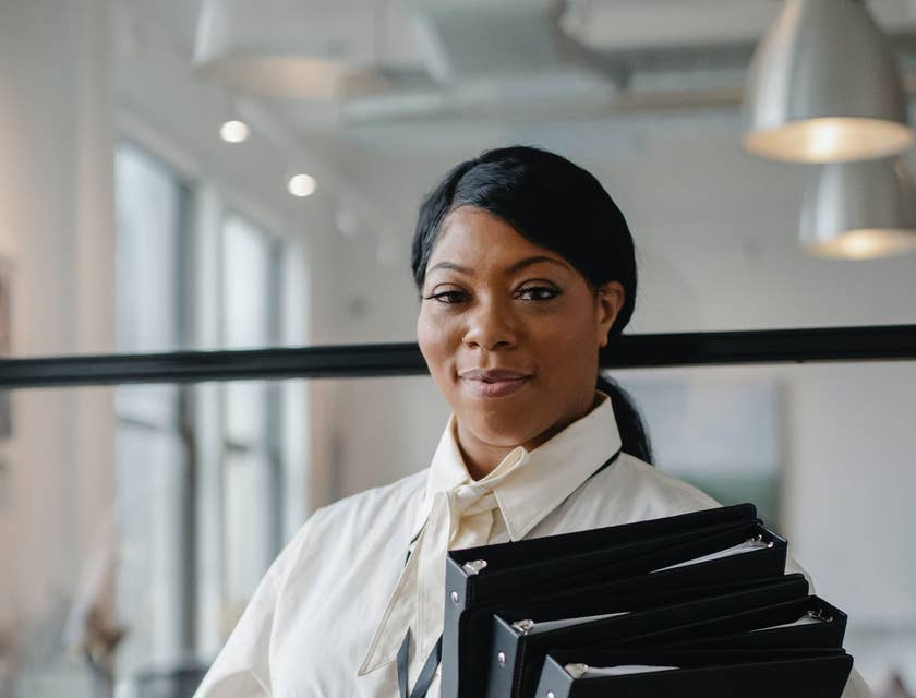 A data entry specialist in a white shirt holding a stack of black files.