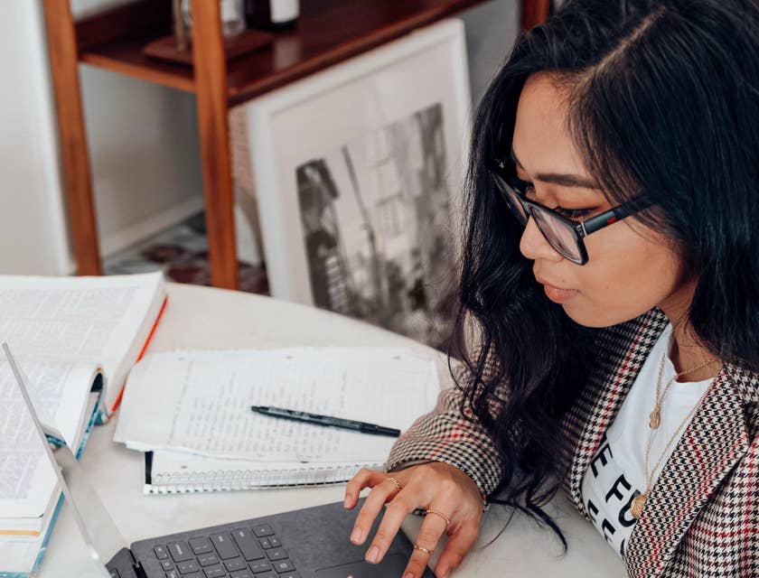 Data Entry Typist working on a laptop with notes and and open book on the table