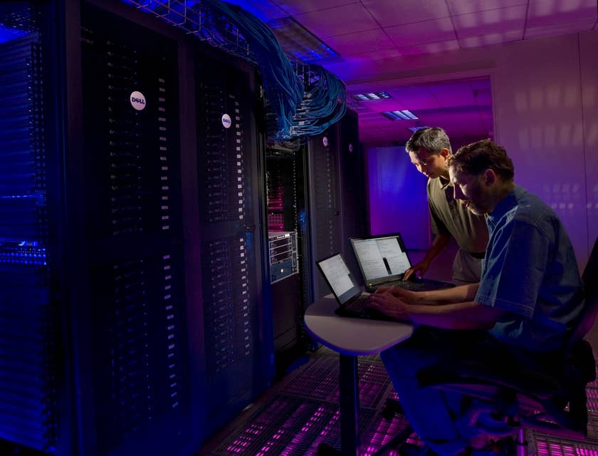 Database Manager working on upgrading the data retrieval system inside the server room while his colleague looks on