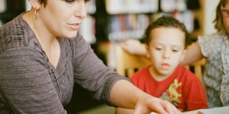 Day care worker turning a page of a book while the children looks on.