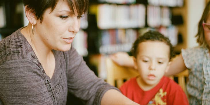 Day care worker turning a page of a book while the children look on.