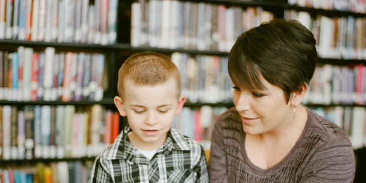 A day care worker with a child in a library.