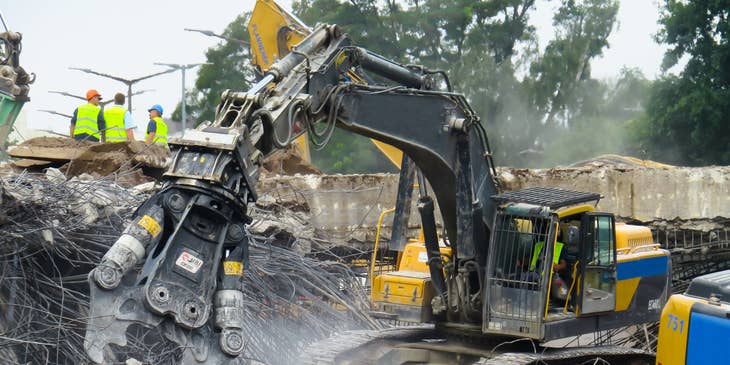 Demolition laborer operating heavy equipment to demolish the building.