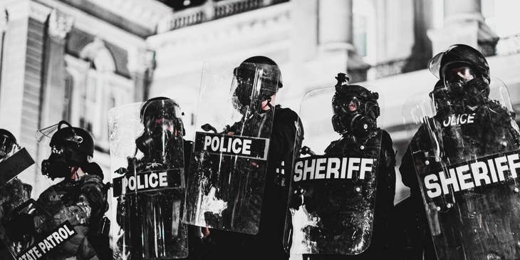 Deputy Sheriff wearing full protective gear and shield while on-duty at a high alert area with the rest of the team