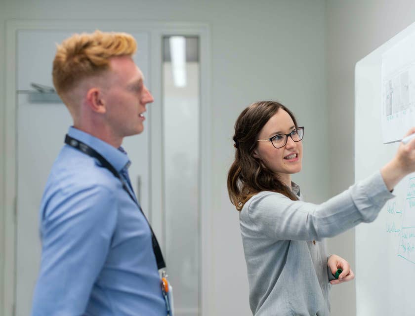 female DevOps Engineer proposing an interface upgrade on the whiteboard while her colleague looks on