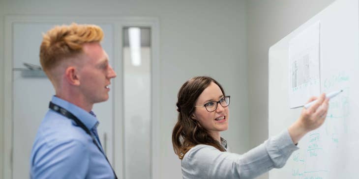female DevOps Engineer proposing an interface upgrade on the whiteboard while her colleague looks on