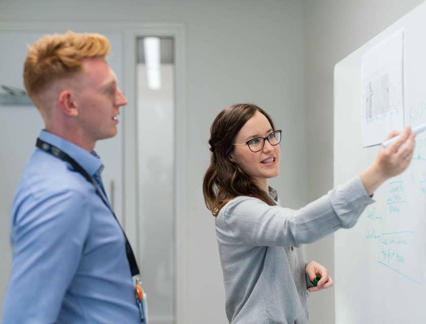 female DevOps Engineer proposing an interface upgrade on the whiteboard while her colleague looks on