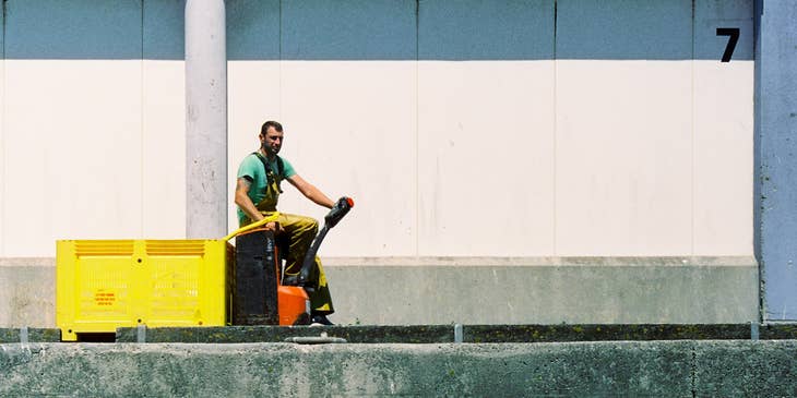 A Dock Worker driving a small equipment on the side of the docks on his way to fetch cargos.