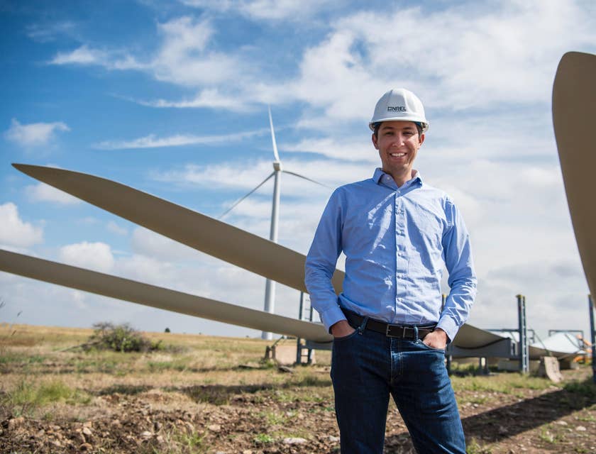 Environmental Engineer wearing a hard hat while standing along the line of wind turbines