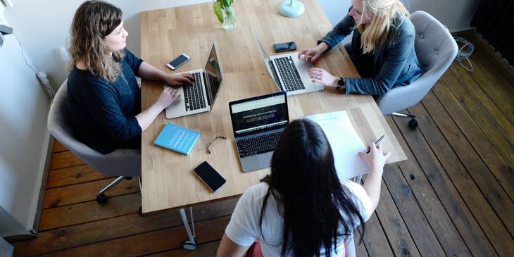 three female Financial Analysts sitting together in an office desk with their laptops open