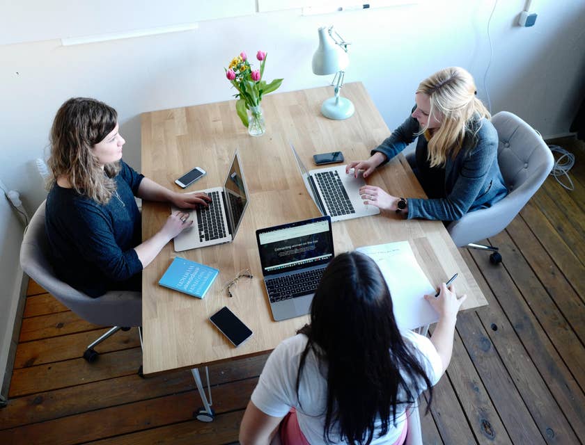 three female Financial Analysts sitting together in an office desk with their laptops open