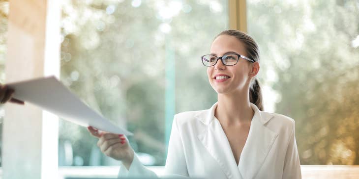 Female financial auditor wearing eyeglasses and handing the business documents to her assistant