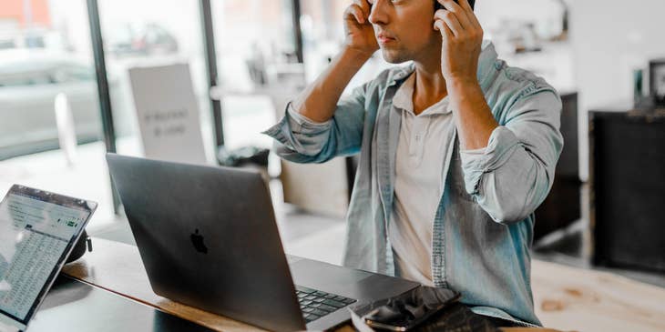 Male financial services representative sitting with his laptop open on a desk while fixing his headset