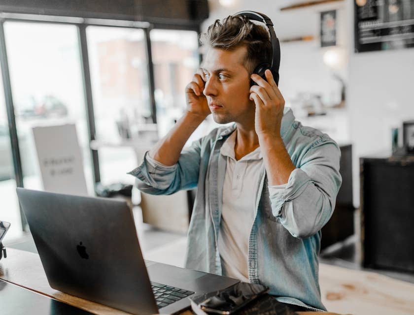 male Financial Services Representative sitting with his laptop open on a desk while fixing his headset