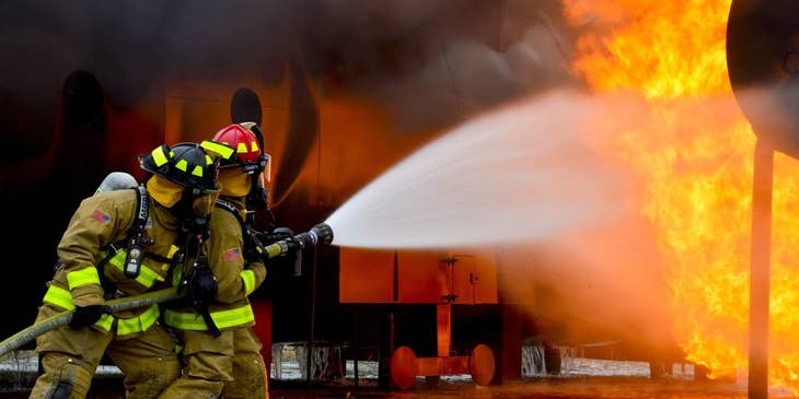 Two firefighters holding a water hose and putting out the blaze on the scene