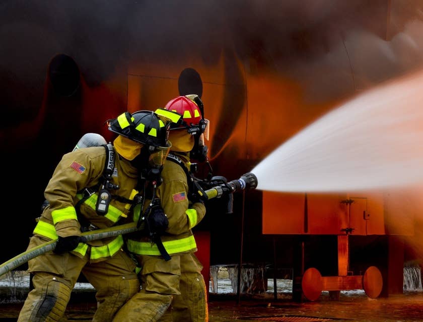 Two firefighters holding a water hose and putting out the blaze on the scene