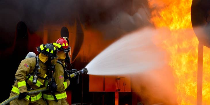 two Firefighters holding a water hose and putting out the blaze on the scene