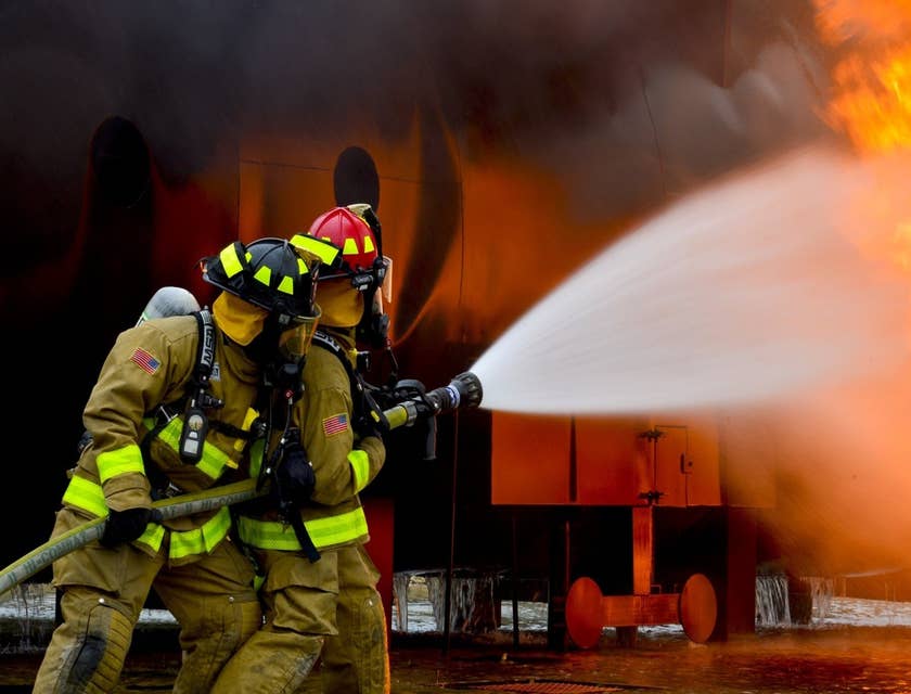 two Firefighters holding a water hose and putting out the blaze on the scene