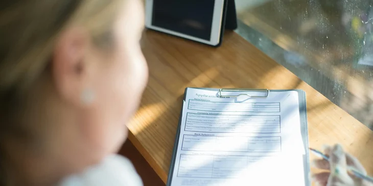 Una mujer en un abrigo beige llenando un formulario de solicitud de trabajo.