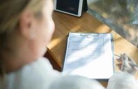 Una mujer en un abrigo beige llenando un formulario de solicitud de trabajo.