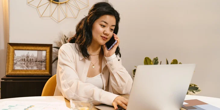 A freelancer talking to a client over the phone while typing on a laptop.
