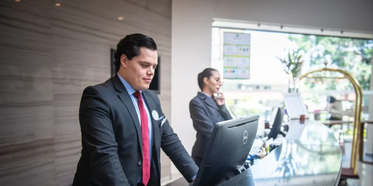 A male front desk manager with his staff at the reception area.